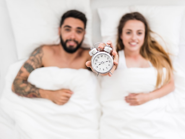 Young couple lying on bed showing alarm clock