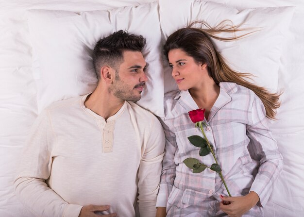 Young couple lying in bed with rose 