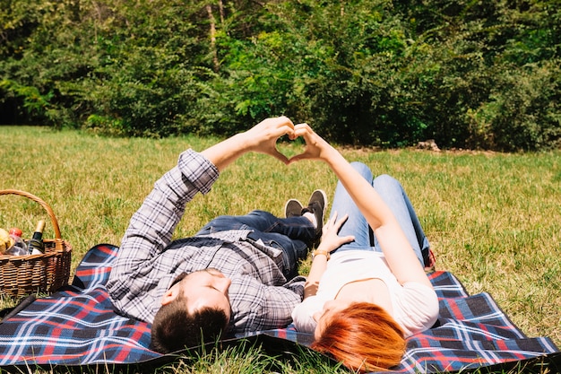 Free photo young couple lying on blanket making heart shape with hands in the park