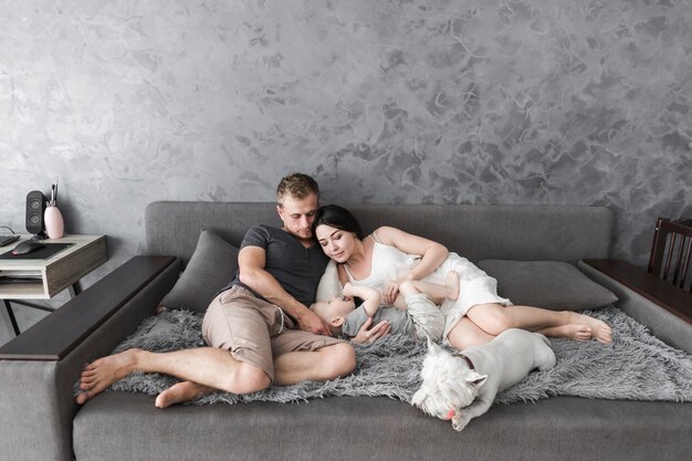 Young couple lying with their cute son and dog on sofa