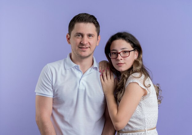 Young couple man and woman standing together happy in love over blue wall