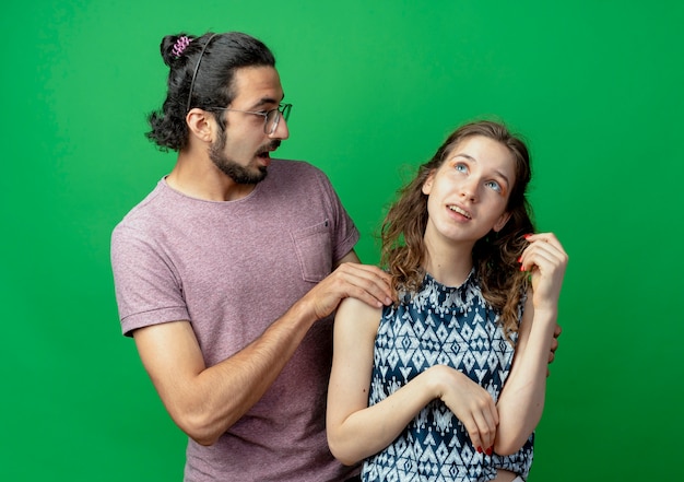 Free Photo young couple man and woman, surprised man touching shoulder of her girlfriend which standing with pensive expression standing over green background