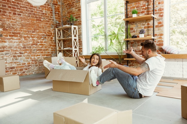 Free photo young couple moved to a new house or apartment. having fun with cardboard boxes, relaxing after cleaning and unpacking at moved day. look happy. family, moving, relations, first home concept.