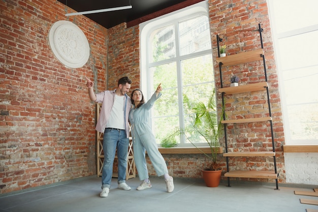 Young couple moved to a new house or apartment. Look happy and confident. Family, moving, relations, first home concept. Thinking about future repair and relaxing after cleaning and unpacking.