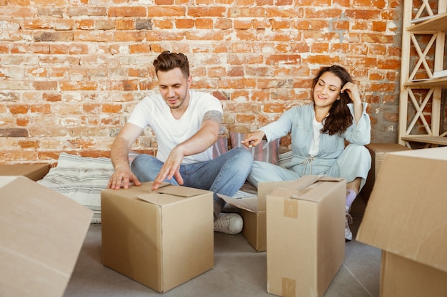 Free photo young couple moved to a new house or apartment. unpacking cardboard boxes together, having fun at moved day. look happy, dreamful and confident. family, moving, relations, first home concept.