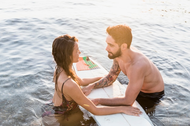 Young couple near surfboard in sea