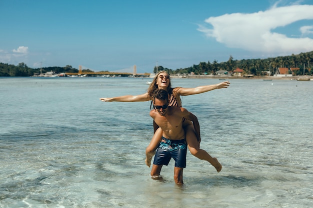 Free Photo young couple posing on the beach, having fun in the sea, laughing and smiling