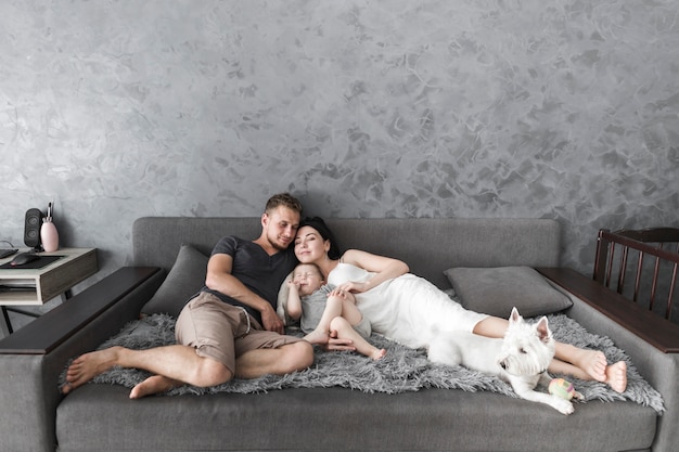 Free Photo young couple relaxing on sofa with their son and white dog