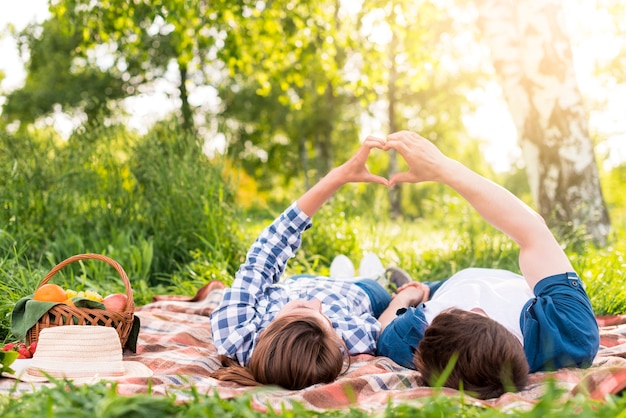 Free photo young couple resting on plaid and showing heart gesture