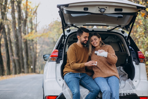 Young couple sitting at the back of a car drinking tea in forest