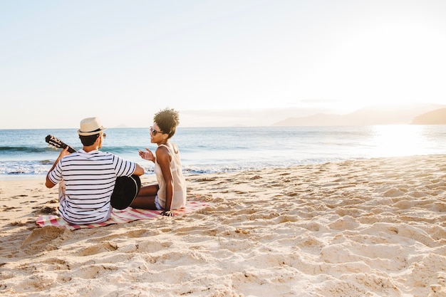 Young couple sitting at the beach and playing the guitar