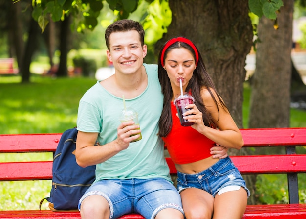 Young couple sitting on bench drinking healthy smoothies in the park