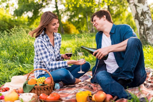 Young couple sitting on blanket and pouring wine