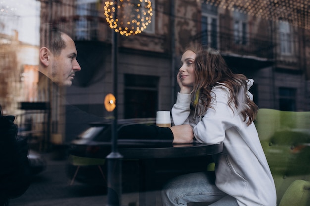 Young couple sitting in a cafe behind the window