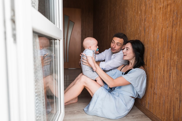 Young couple sitting on floor near the window playing with their baby