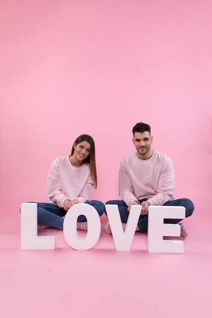 Free photo young couple sitting near big love sign