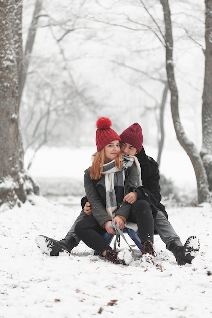 Free photo young couple sitting on sleigh and playing with snow