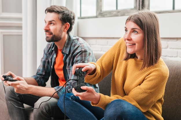 Free photo young couple sitting on sofa enjoying playing the video game