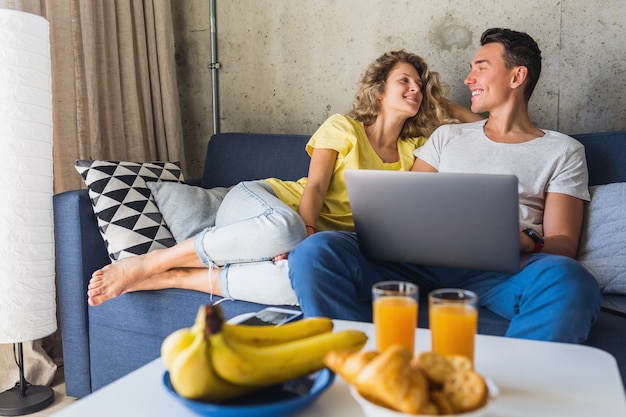 Young couple sitting on sofa at home looking in laptop