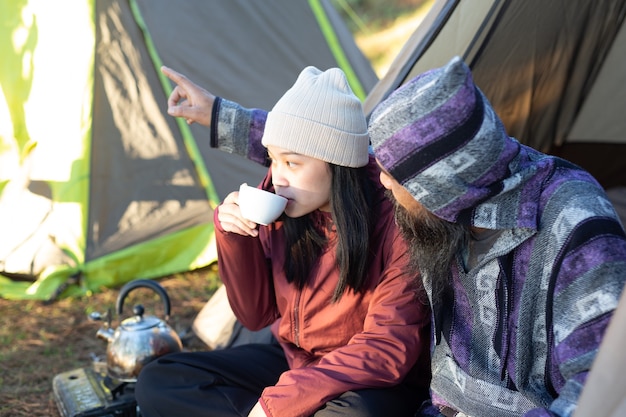 Young couple sitting in the tent and drinking coffee in the morning