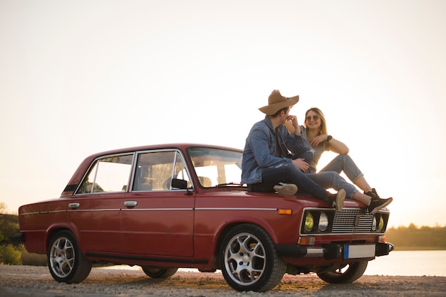 Free Photo young couple sitting on a vintage car