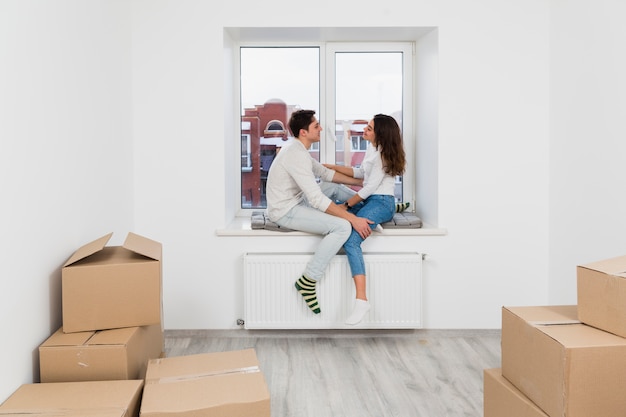 Young couple sitting on window sill enjoying in new apartment