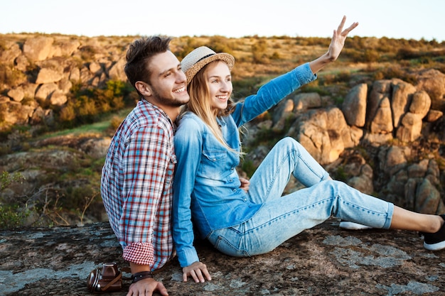 Free photo young couple smiling, sitting on rock in canyon, enjoying view