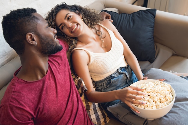 Young couple spending time together and watching tv series or movies while sitting on couch at home.