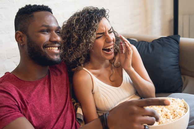 Young couple spending time together and watching tv series or movies while sitting on couch at home.