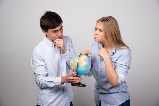 Young couple standing with an Earth globe on gray wall