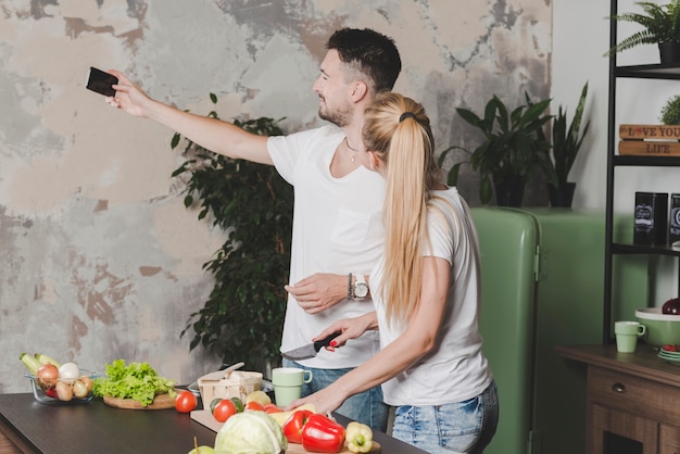 Free photo young couple taking selfie on mobile phone while cutting vegetables