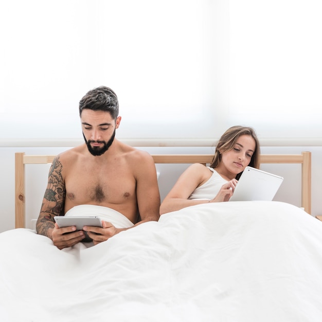 Free photo young couple using digital tablet on bed