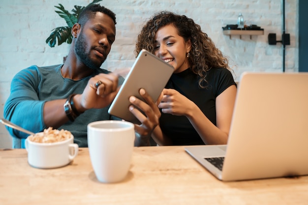 Free photo young couple using a digital tablet and a laptop while having breakfast together at home.