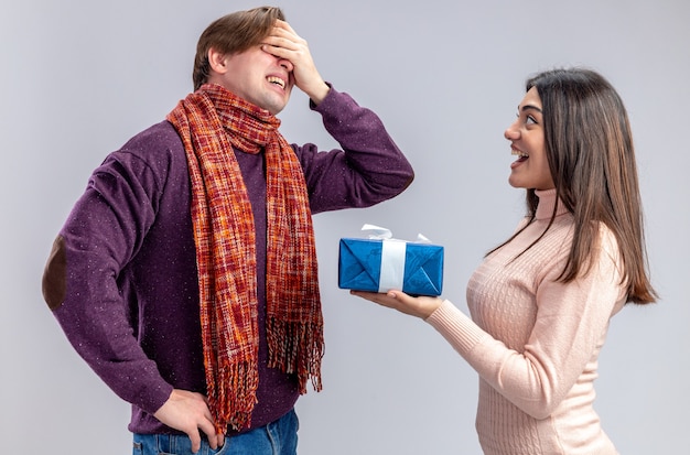 Young couple on valentines day excited girl giving gift box to regretted guy isolated on white background