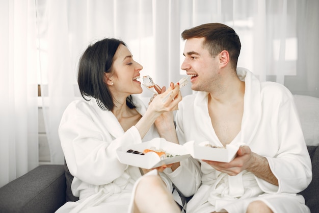 Young couple wearing bathrobes eating sushi.