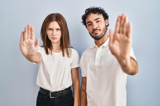 Young couple wearing casual clothes standing together doing stop sing with palm of the hand. warning expression with negative and serious gesture on the face.