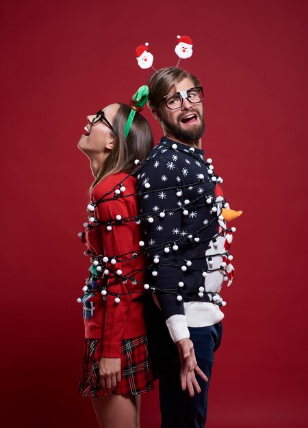 Young couple in weird Christmas clothes tied with Christmas lights