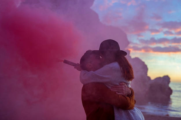 Free photo young couple with smoke bomb kissing on sea shore