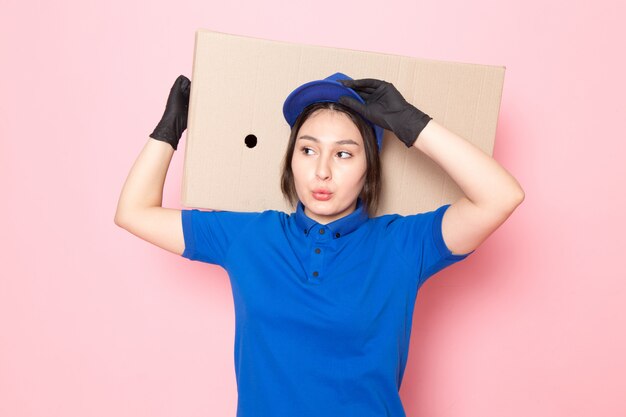 young courier in blue polo blue cap jeans holding package on pink