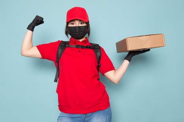 young courier in red polo red cap black sterile protective mask black backpack holding package on blue