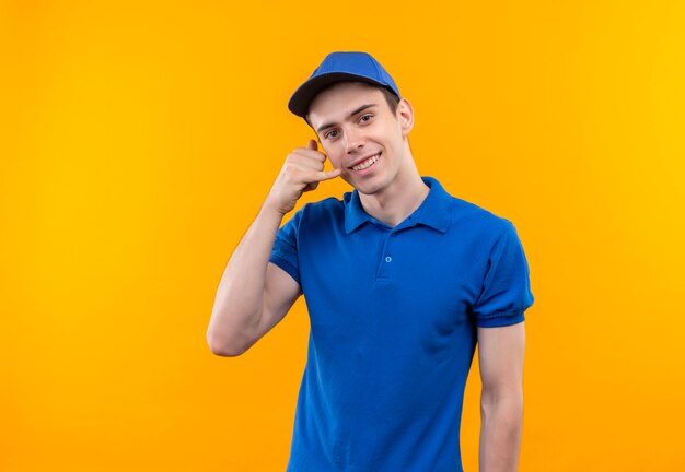 Young courier wearing blue uniform and blue cap doing happy call me with hand