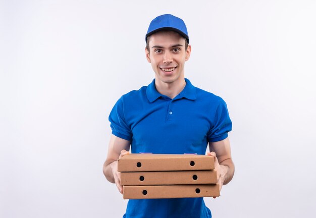 Young courier wearing blue uniform and blue cap smiles and holds boxes