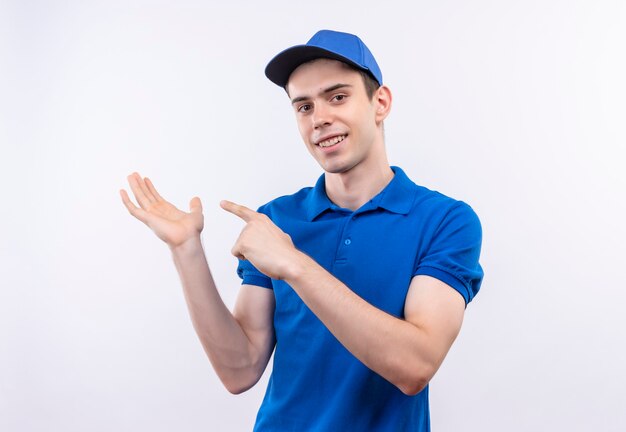 Young courier wearing blue uniform and blue cap smiles and points on his hand