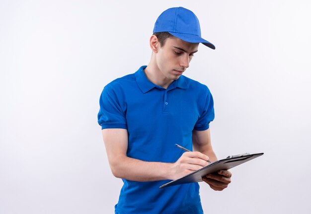 Young courier wearing blue uniform and blue cap writes on a clipboard