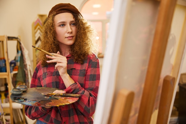 Young curly artist holds a brush and  is drawing a picrure