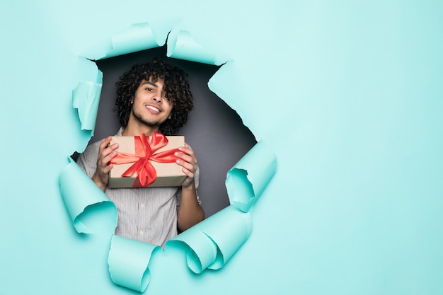 Free Photo young curly handsome man holding gift from hole on green paper