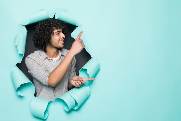 Free Photo young curly handsome man pointed on side from hole on green paper