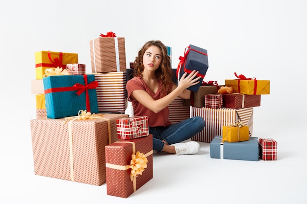 Free Photo young curly woman sitting on floor among gift boxes guessing what is inside