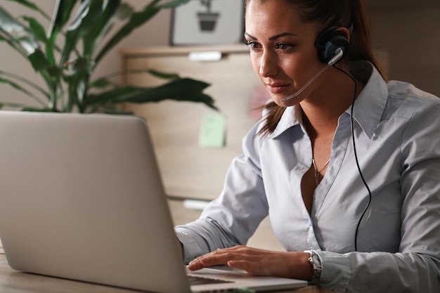 Young customer support agent with headset working on laptop in a call center