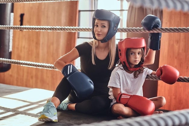 Free Photo young cute girl in helmet and her beautiful female boxing trainer are posing for photographer on the ring.